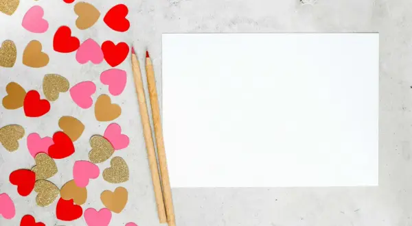 Cœurs rouges, roses et dorés pour une **journée Saint-Valentin** à écrire sur une feuille blanche avec deux crayons.