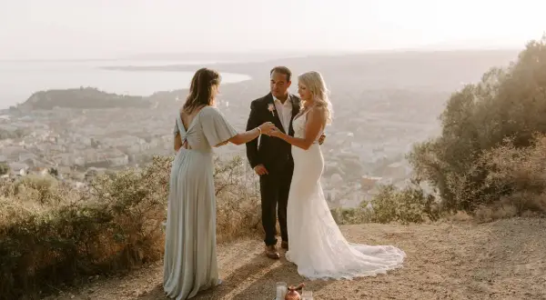 Cérémonie d'elopement mariage intime au sommet d'une colline, avec vue sur une ville et la mer. Le couple échange ses vœux, officiés par une amie.