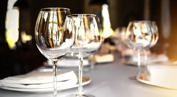 Trois verres à vin vides sur une table dressée, prêts pour un repas. Chaque verre reflète la lumière, comme un marque place verre.