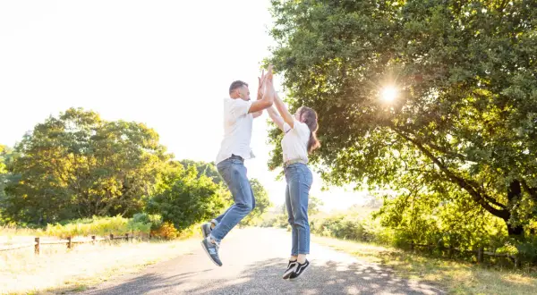 Un couple saute de joie sur un chemin ensoleillé, une belle photo d'engagement dans la nature.