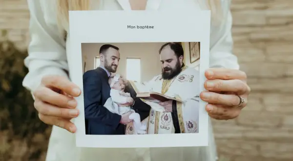 Carte "Mon baptême" tenue par des mains. Photo d'un bébé pleurant, tenu par son père, recevant le baptême d'un prêtre. Un beau texte baptême pour les grands-parents.