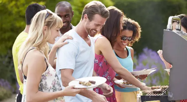 Des amis profitent d'un barbecue pour mariage en plein air, avec des brochettes et du maïs grillé.