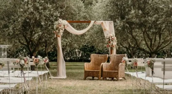 Un décor champêtre pour une célébration laïque : chaises blanches, arche fleurie, fauteuils en rotin sous les oliviers.