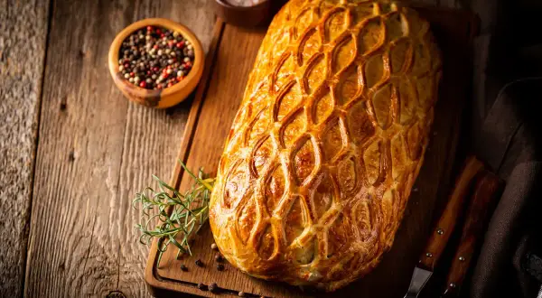 Un rôti en croûte dorée, prêt pour un menu de baptême à préparer la veille. Poivre et romarin à proximité.
