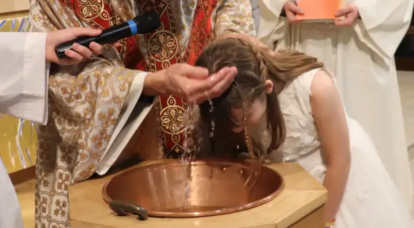 Cérémonie de baptême d'enfants : un prêtre verse de l'eau sur la tête d'une jeune fille dans une église.