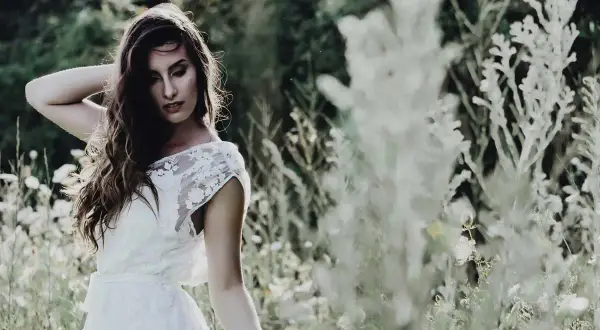 Une mariée en robe blanche, cheveux longs et ondulés, pose dans un champ fleuri. Ambiance romantique pour un mariage bohème.