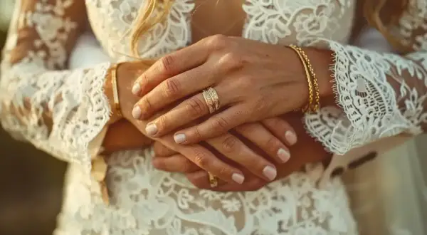 Mains jointes, alliances étincelantes sur une robe de mariée en dentelle. L'image évoque de beaux textes pour un mariage civil, symbolisant l'union et l'amour éternel.