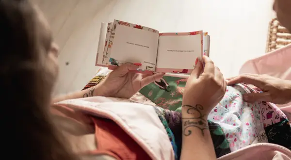Un livre ouvert avec des messages tendres, comme un texte pour mon filleul. Les mains tiennent le livre, entourées de tissus colorés.