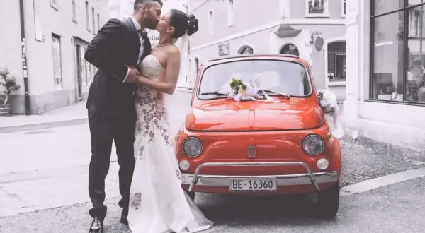Un couple s'embrasse devant une Fiat 500 rouge décorée, un doux souvenir de leur mariage à deux à l'étranger.