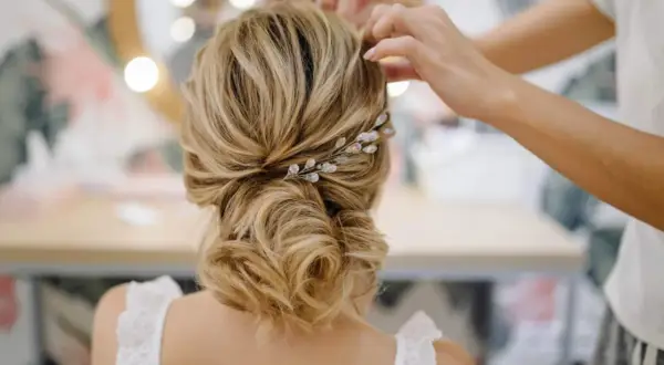 Une mariée se fait coiffer des cheveux lâchés, ornés d'une barrette scintillante. Une coiffure mariage cheveux lâchés élégante.