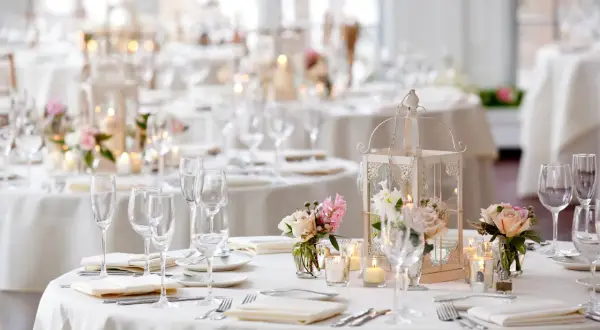 Disposition table mariage élégante avec lanternes, bougies et bouquets de roses. Vaisselle et verres prêts pour les invités.