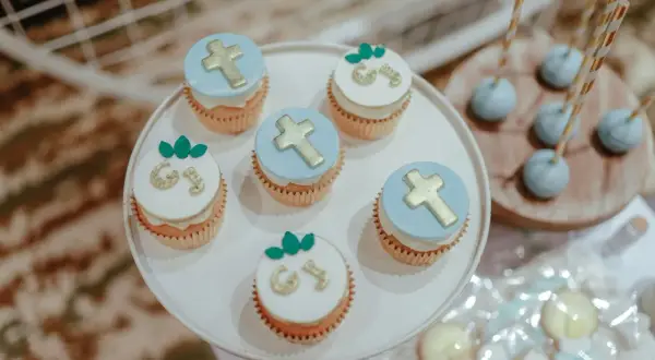 Jolis cupcakes décorés de croix dorées et de lettres pour un menu baptême à faire soi même. Des cake pops bleus sont aussi visibles.