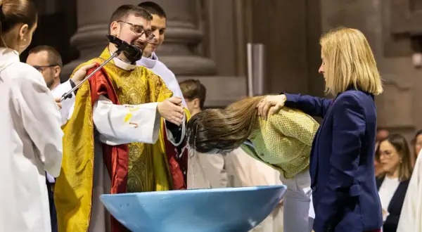 Cérémonie de baptiser en arabe. Un prêtre verse de l'eau sur la tête d'une femme dans un bassin bleu.