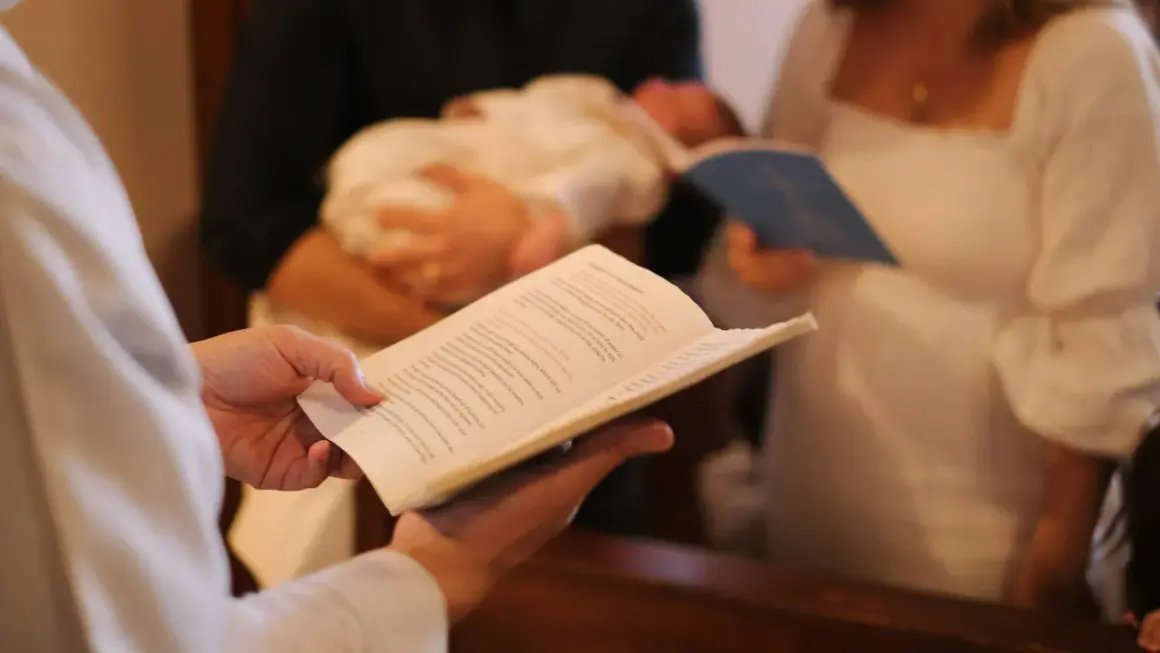 Célébration d'un baptême : un livre ouvert est tenu, un bébé est porté, et des parents écoutent attentivement la bénédiction.