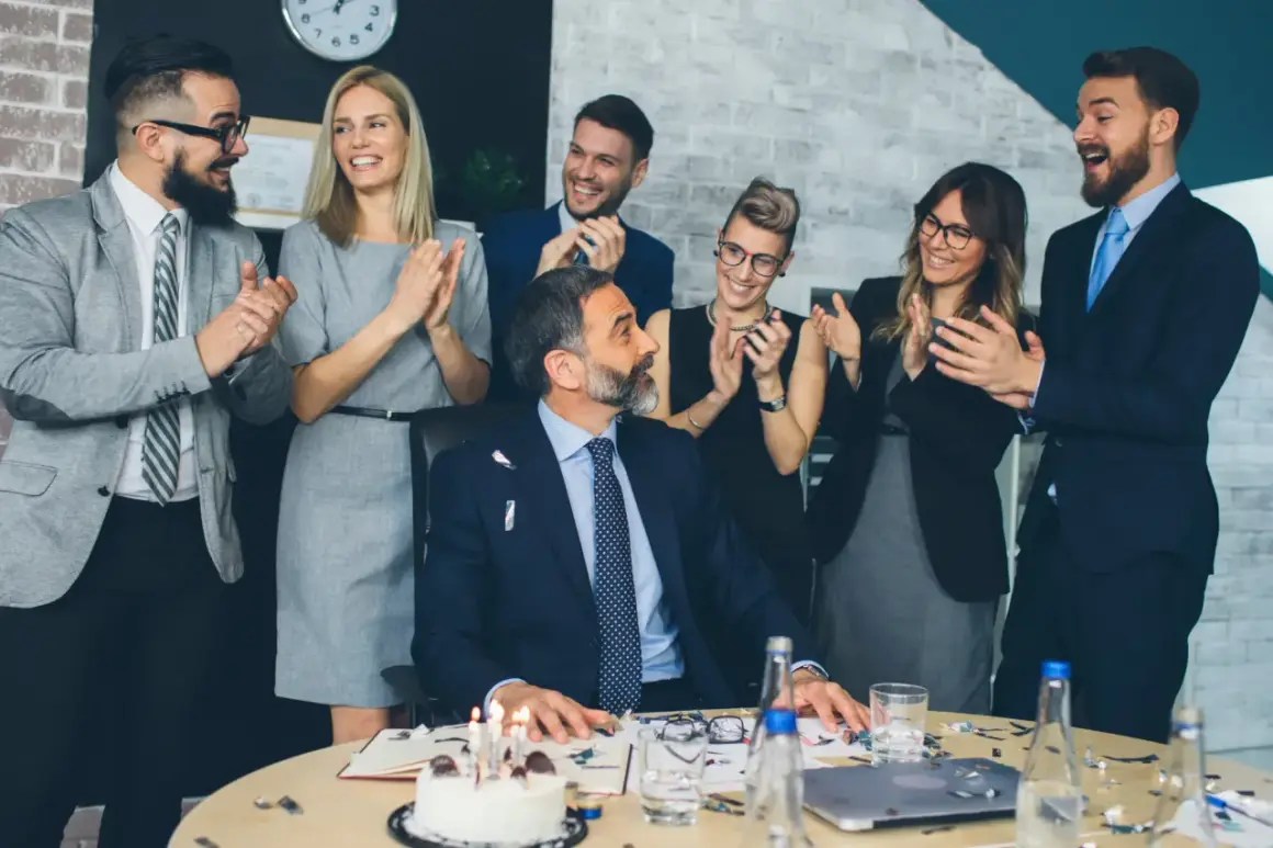 Une équipe célèbre le départ à la retraite de son collègue avec un gâteau et des applaudissements. Un texte invitation départ retraite humoristique serait parfait pour cette occasion !