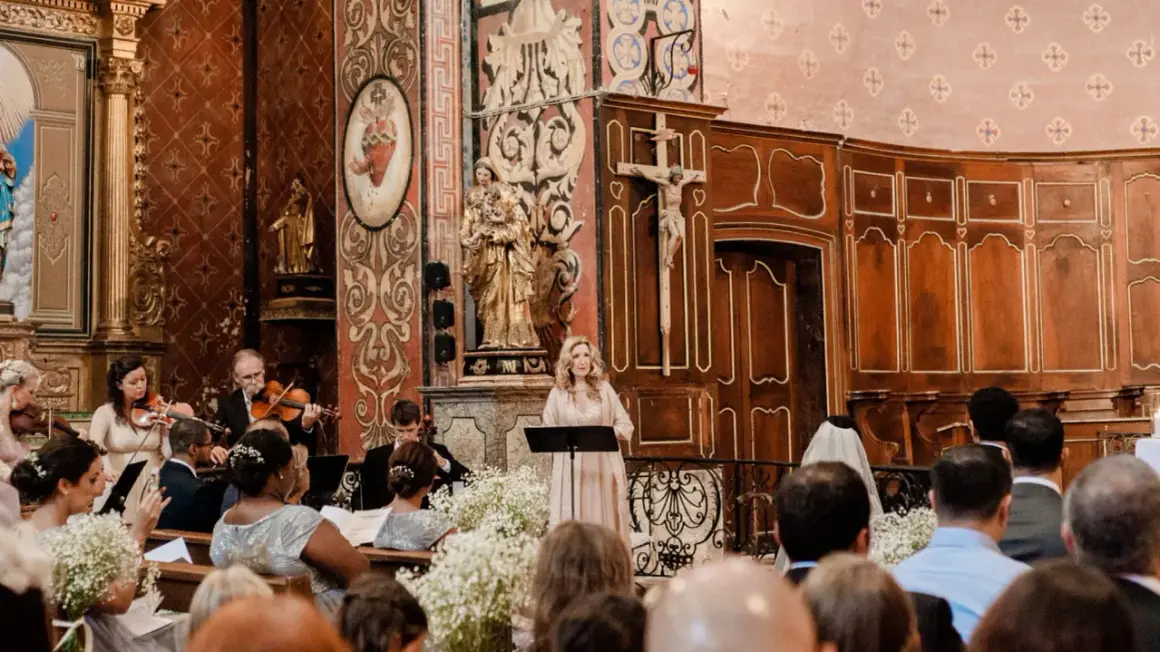 Une femme chante lors d'un mariage, accompagnée d'un orchestre. La prière universelle du mariage résonne dans l'église ornée.