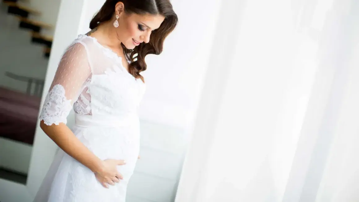 Une future mariée enceinte, vêtue d'une robe blanche, caresse son ventre avec tendresse.