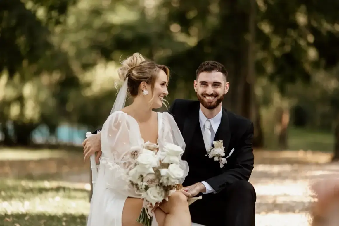 Un couple rayonnant, le marié en costume noir, la mariée en robe blanche, échangeant des regards complices lors de leur échange de voeux mariage.