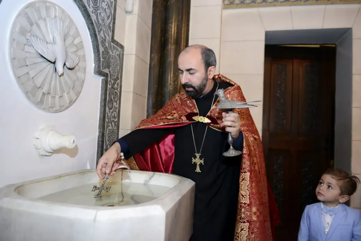 Un prêtre bénit l'eau pour un baptême arménien, un jeune garçon en costume bleu observe attentivement.