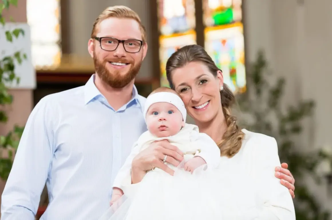 Un couple souriant pose avec leur bébé lors d'un baptême. La question "peut-on être marraine à 11 ans ?" résonne, mais ici, c'est une famille unie.