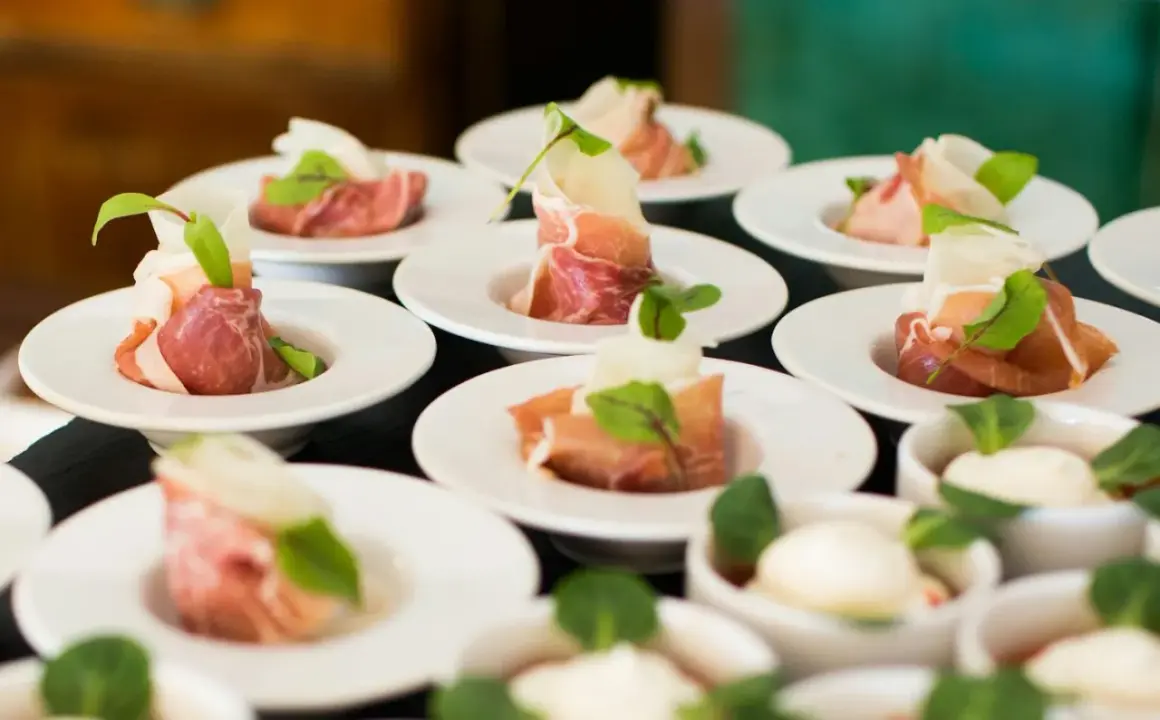 Petits amuse-bouches de jambon cru roulé, melon et garniture verte, prêts pour un dîner assis.