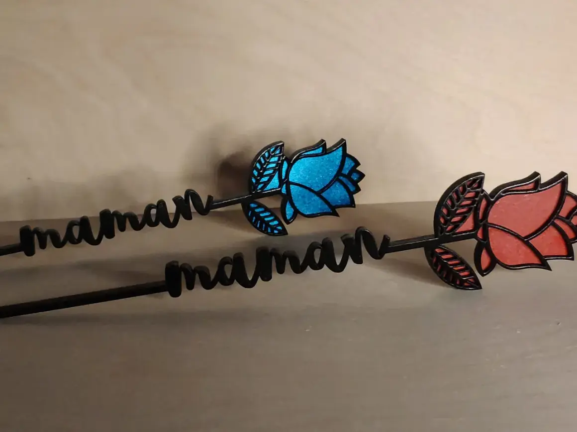 Deux roses décoratives avec le prénom "maman" gravé, l'une bleue, l'autre rouge.