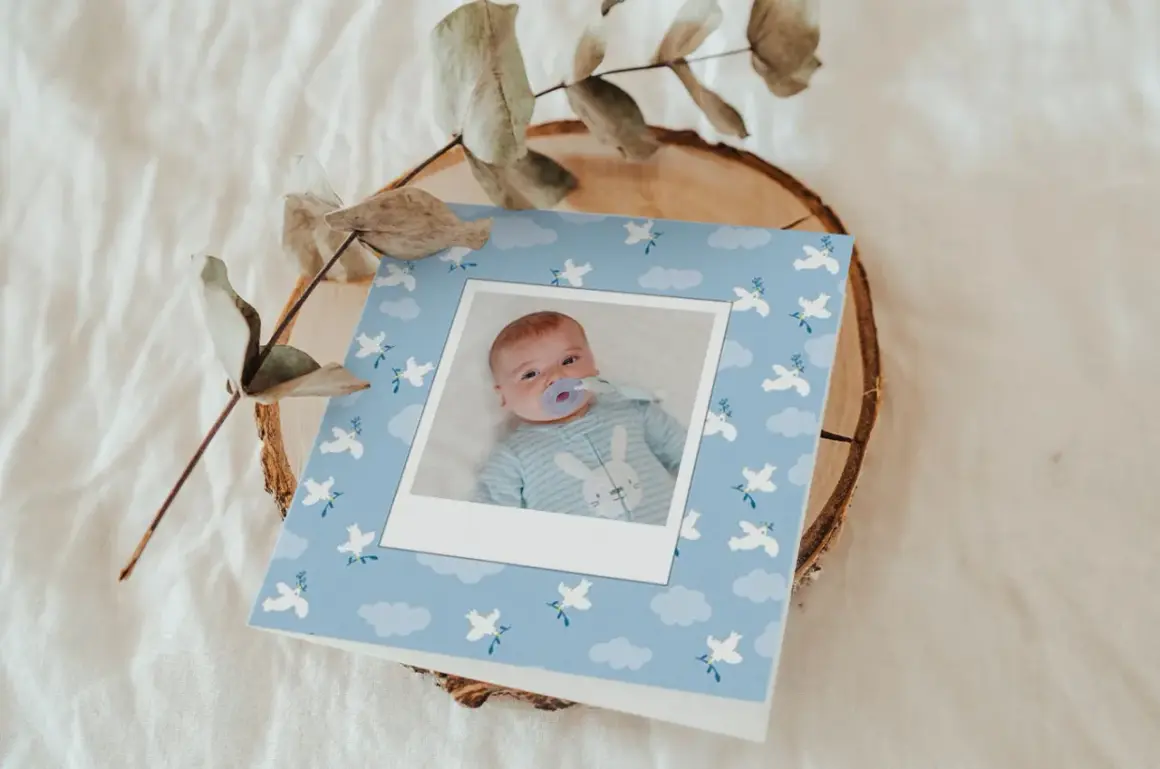 Carte de baptême originale pour un garçon, avec une photo de bébé sur fond bleu ciel orné de colombes et de nuages.