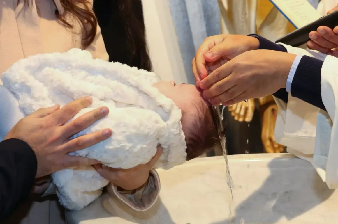 Cérémonie de baptême en hiver. Un bébé est tenu par ses parents, une main verse de l'eau sur sa tête.