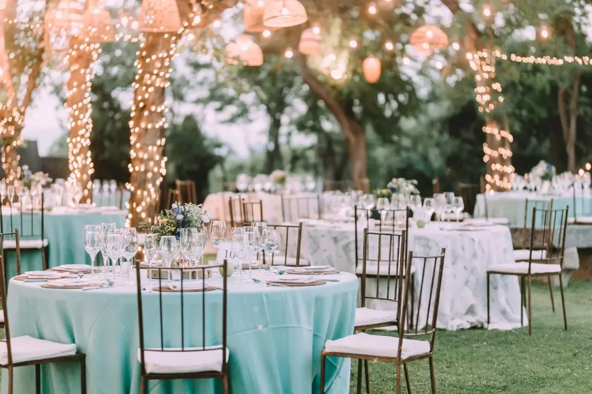 Tables dressées pour un mariage jardin féerique, éclairées par des guirlandes lumineuses dans les arbres.