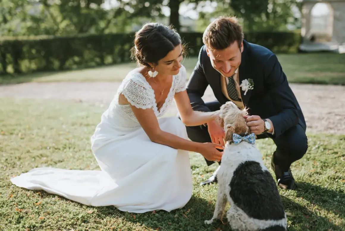 Un couple heureux lors d'un mariage campagne, caressant leur chien portant un nœud papillon bleu.