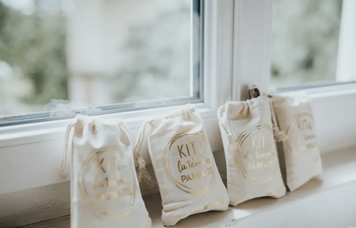 Quatre petits sacs en tissu écru, chacun portant l'inscription dorée "KIT du témoin PARFAIT". Un cadeau témoin mariage personnalisé, prêt à être offert.