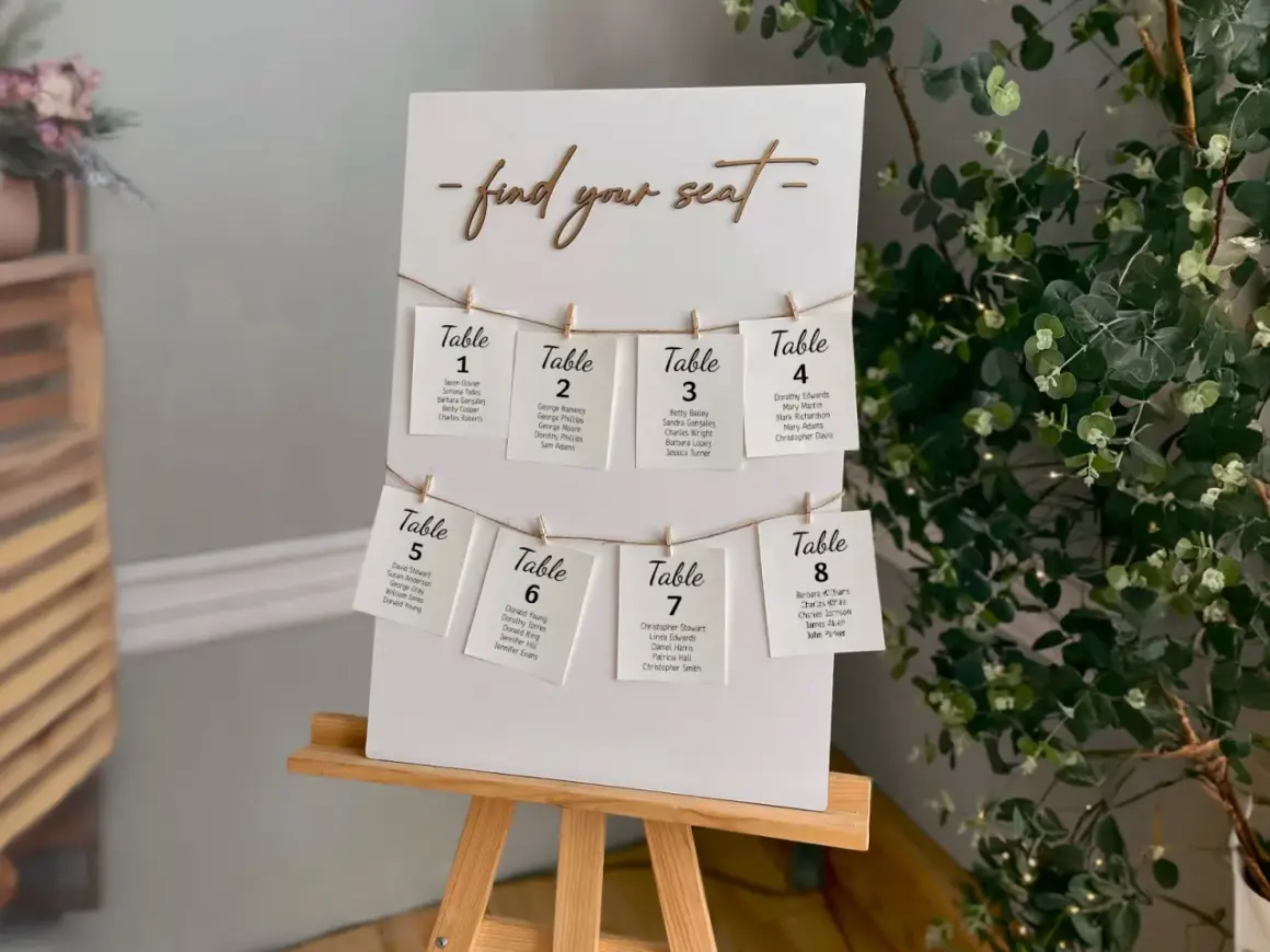 Un panneau "Trouvez votre siège" avec des cartes de table numérotées, chacune avec des noms d'invités. Un marque place vierge est visible sur la carte de la table 8.
