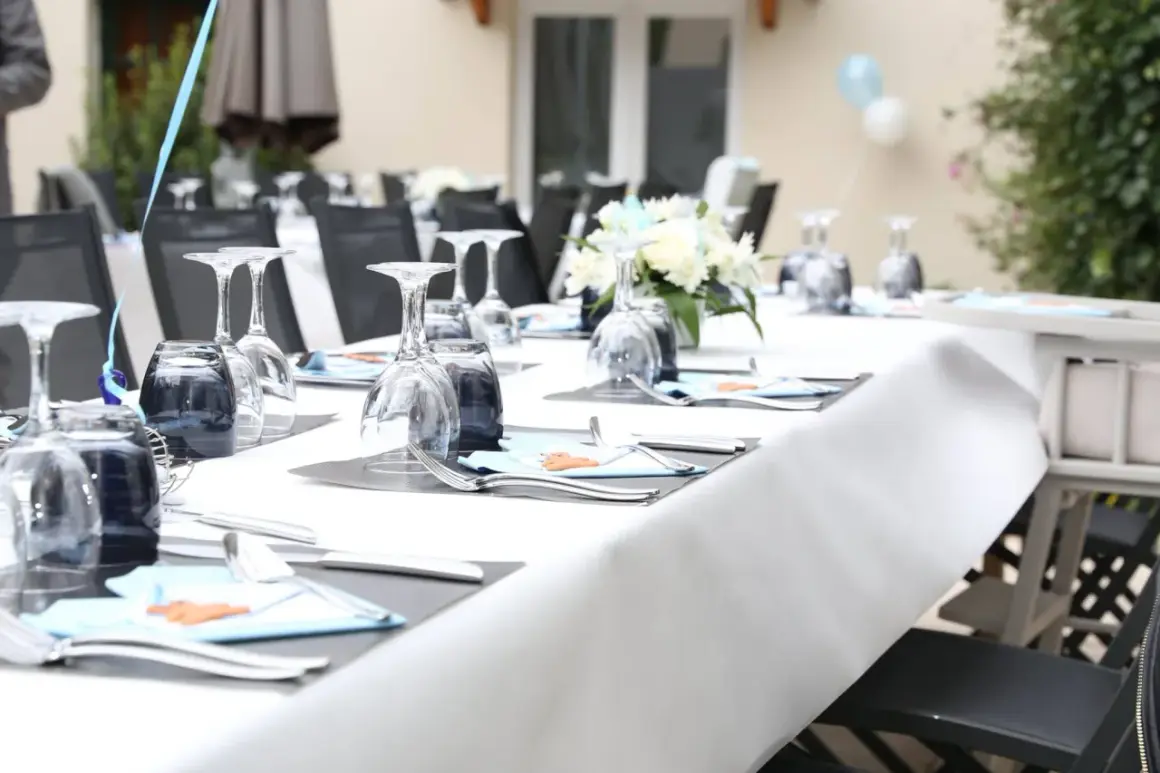 Table dressée pour une fête de baptême, avec des verres, des couverts et des décorations bleues.