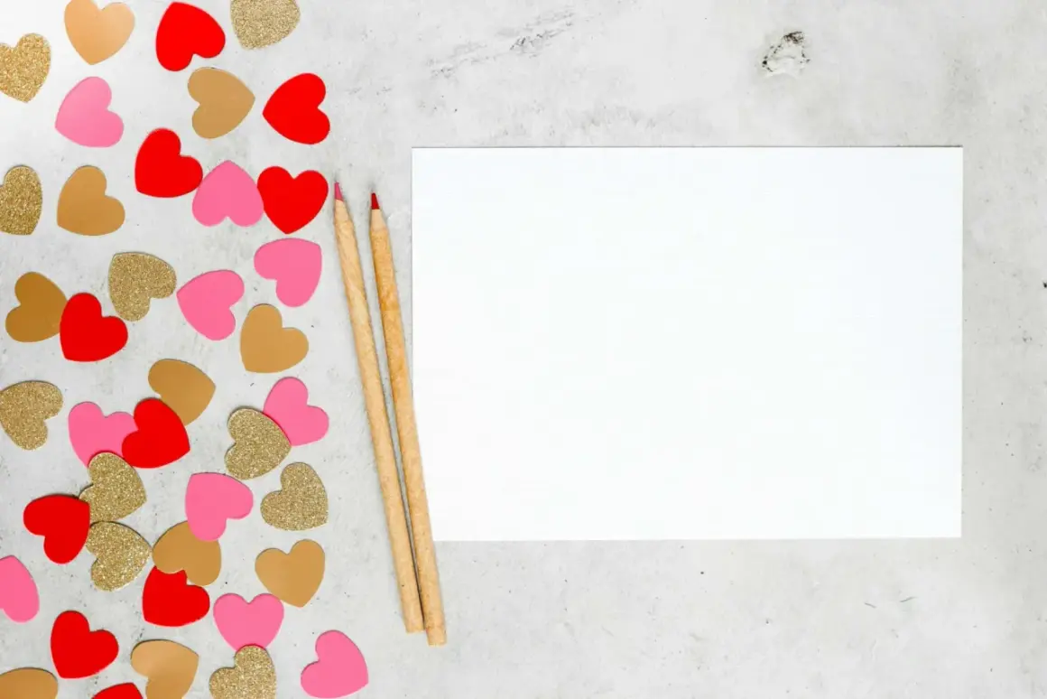 Cœurs rouges, roses et dorés pour une **journée Saint-Valentin** à écrire sur une feuille blanche avec deux crayons.