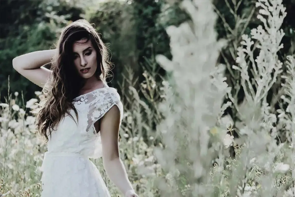 Une mariée en robe blanche, cheveux longs et ondulés, pose dans un champ fleuri. Ambiance romantique pour un mariage bohème.