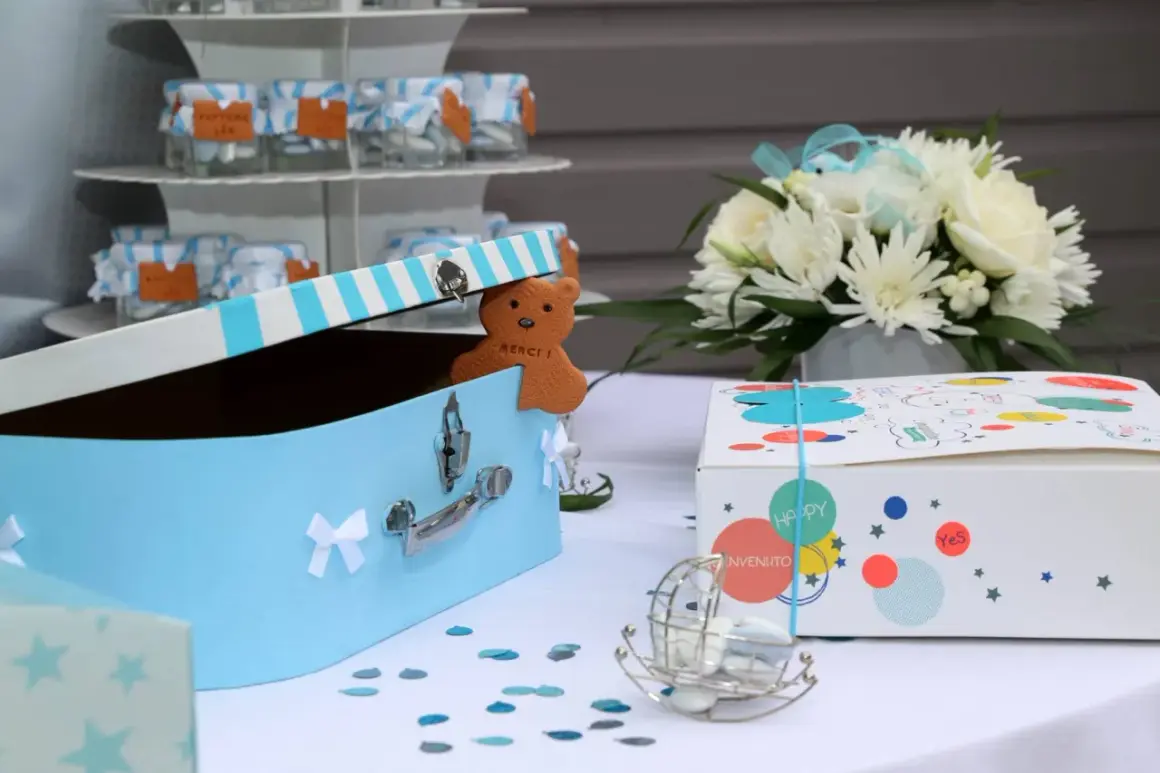 Décoration pour organiser un baptême : boîte à trésors bleue, ours en biscuit "Merci", fleurs blanches et boîtes cadeaux colorées.