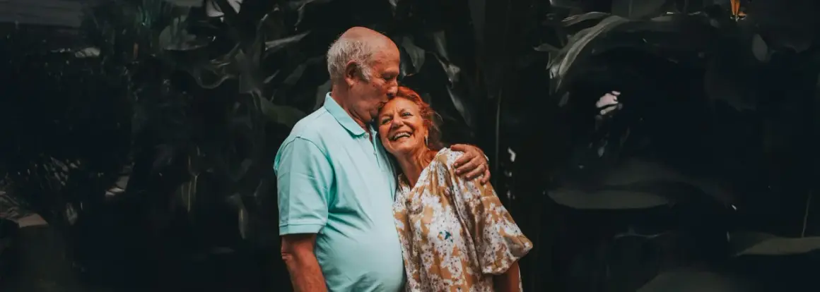 Un couple âgé s'embrasse tendrement, un moment de joie pour fêter sa retraite en famille.