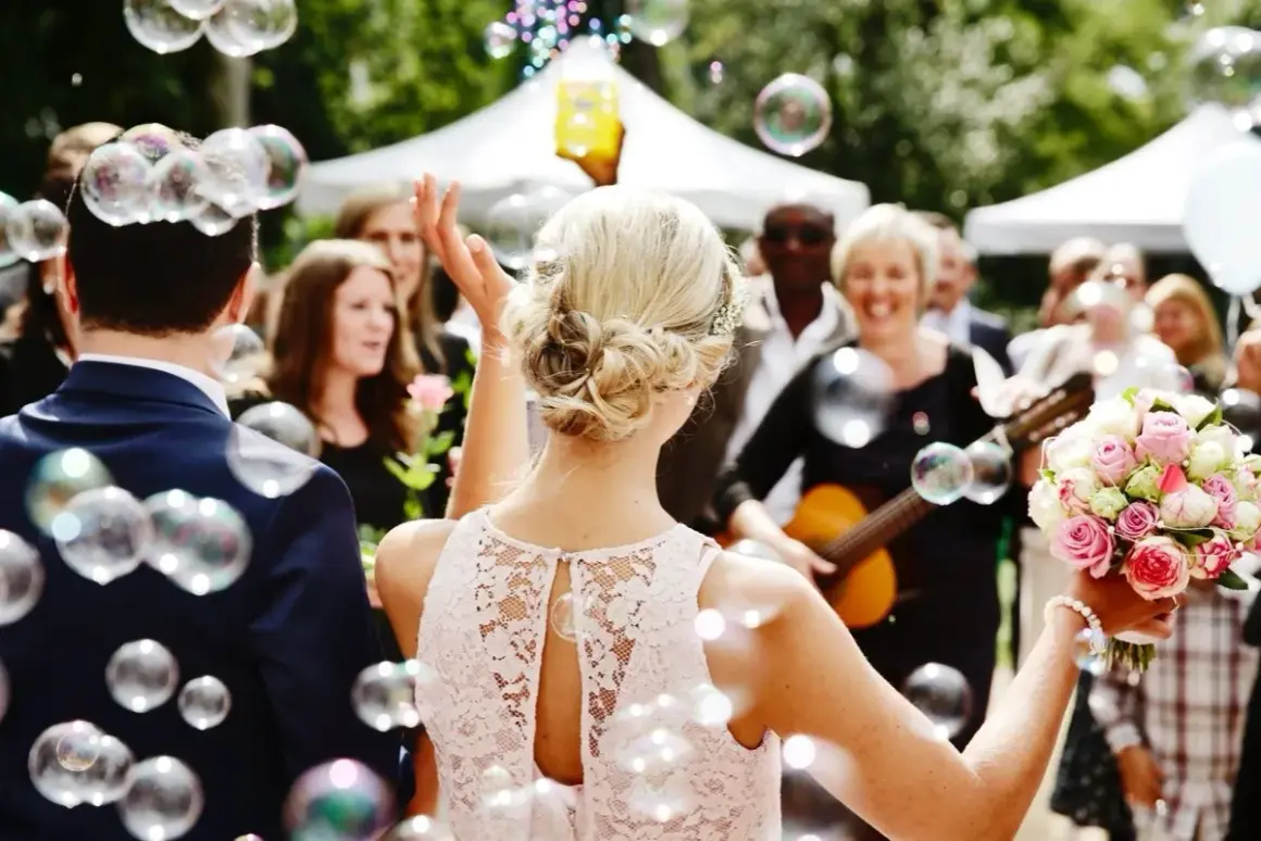 Une marraine, entourée de bulles, tient un bouquet de roses. Une femme joue de la guitare en arrière-plan.