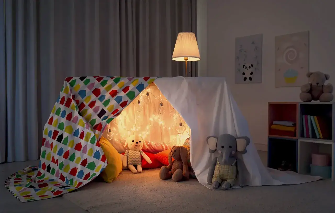 Une tente douillette avec des guirlandes lumineuses, des peluches et un plaid coloré. Parfait pour savoir comment organiser une soirée pyjama mémorable.