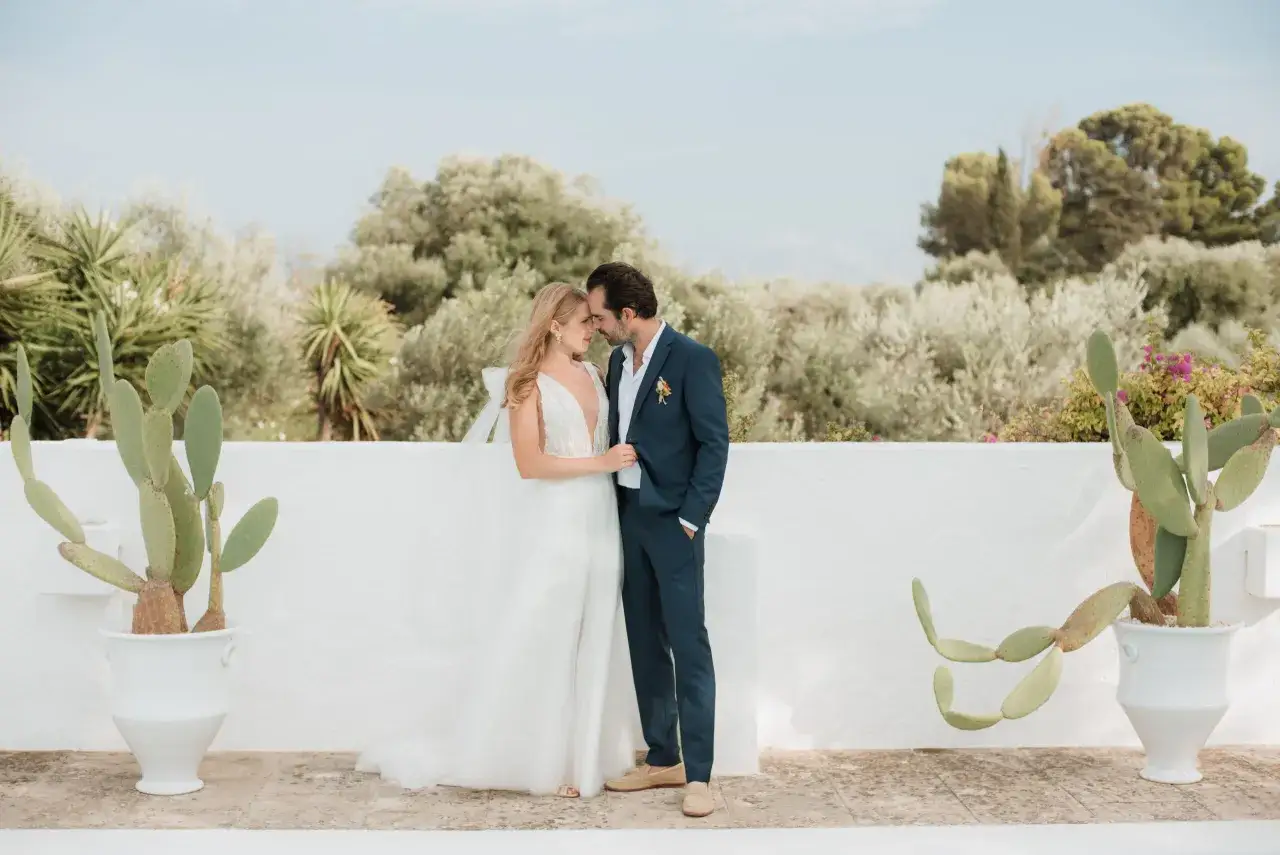 Un couple de jeunes mariés, enlacés tendrement, scelle leur amour. L'échange de leurs vœux de mariage se déroule sous un ciel bleu, entouré de verdure luxuriante et de cactus.