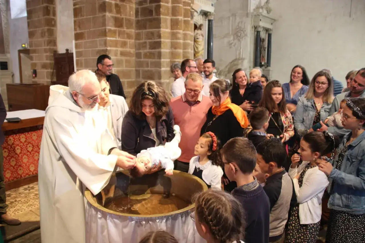 Cérémonie de messe bapteme dans une église. Un prêtre verse de l'eau sur un bébé dans une cuve baptismale, entouré de sa famille et d'invités.