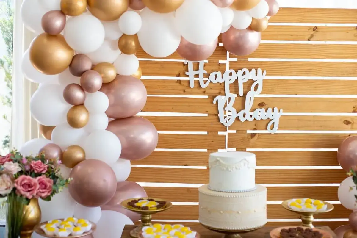 Décoration élégante pour un thème anniversaire adulte : ballons dorés, blancs et rose gold, un gâteau chic et des douceurs.