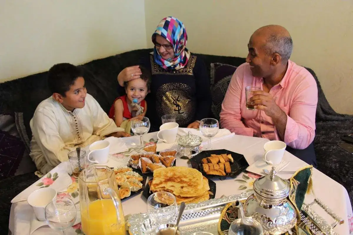 Une famille célèbre la fete de l'aid autour d'une table garnie de pâtisseries et de jus.
