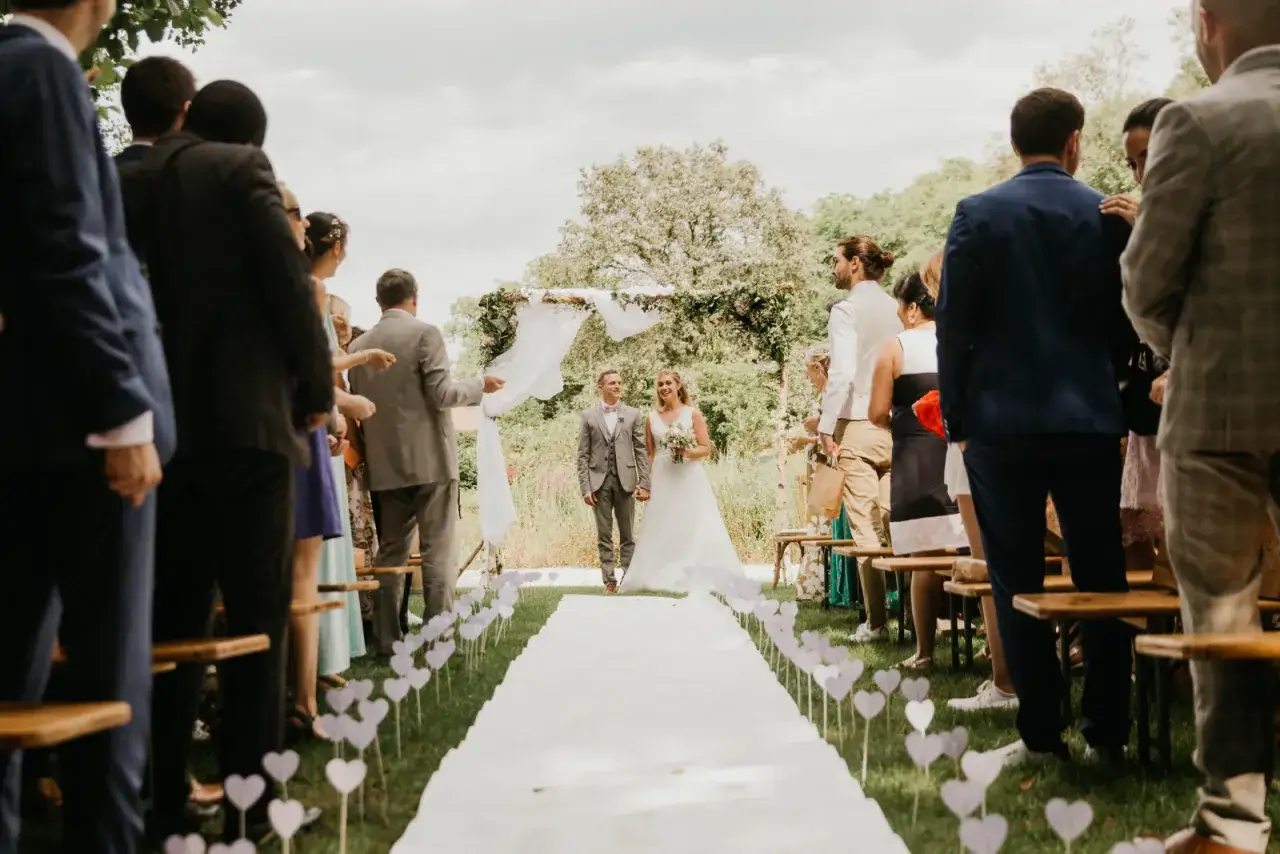 Un couple de mariés marche sur un tapis blanc, entouré d'invités, lors d'une cérémonie laïque exemple.