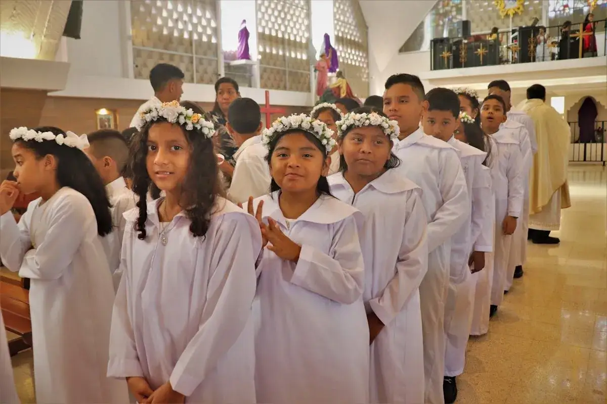 Des enfants en robe blanche et couronnes de fleurs attendent leur baptême chrétien dans une église.