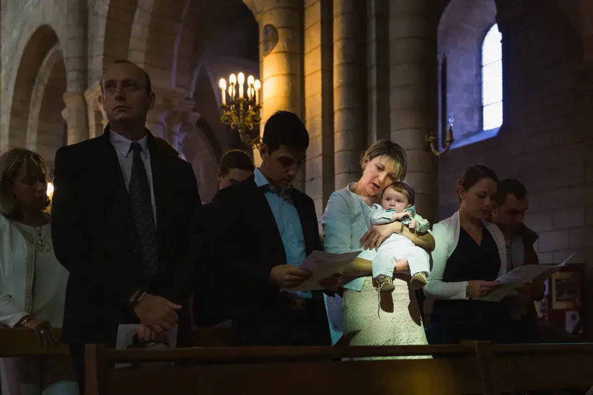 Une famille assiste à un baptême civil ou religieux dans une église. Une mère tient son bébé, entourée de proches.