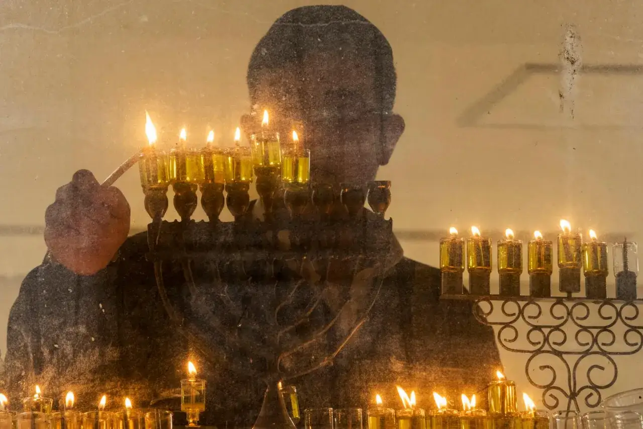 Une main allume une menorah, rappelant l'origine de Hanouka et la lumière qui repousse l'obscurité.