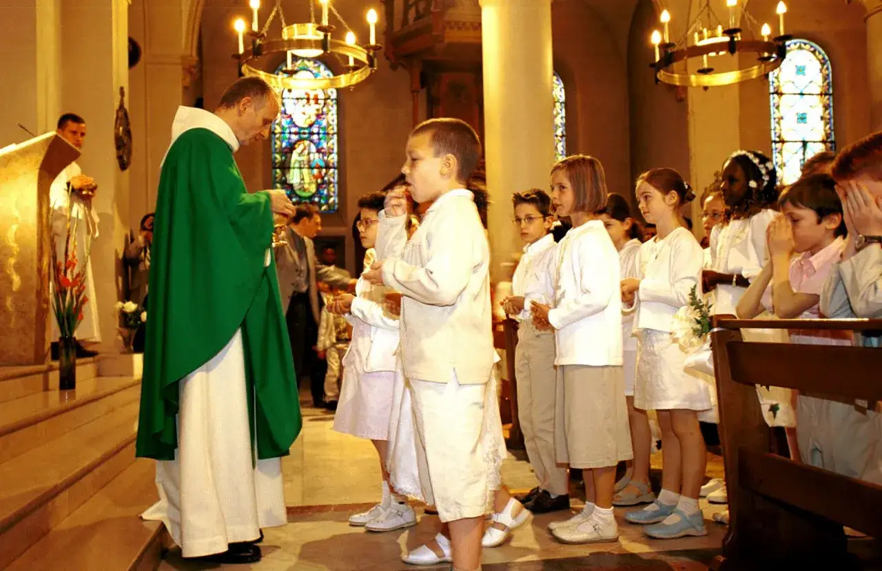 C&eacute;r&eacute;monie de communion dans une &eacute;glise. Un pr&ecirc;tre distribue l'hostie &agrave; des enfants en habits blancs.