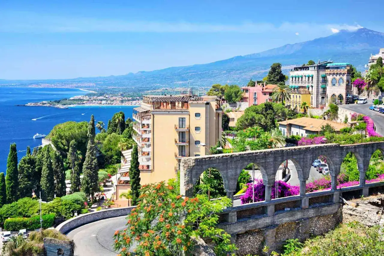 Vue panoramique d'une ville c&ocirc;ti&egrave;re ensoleill&eacute;e, parfaite pour un voyage de noce destination originale. H&ocirc;tels, v&eacute;g&eacute;tation luxuriante et le volcan Etna en arri&egrave;re-plan.