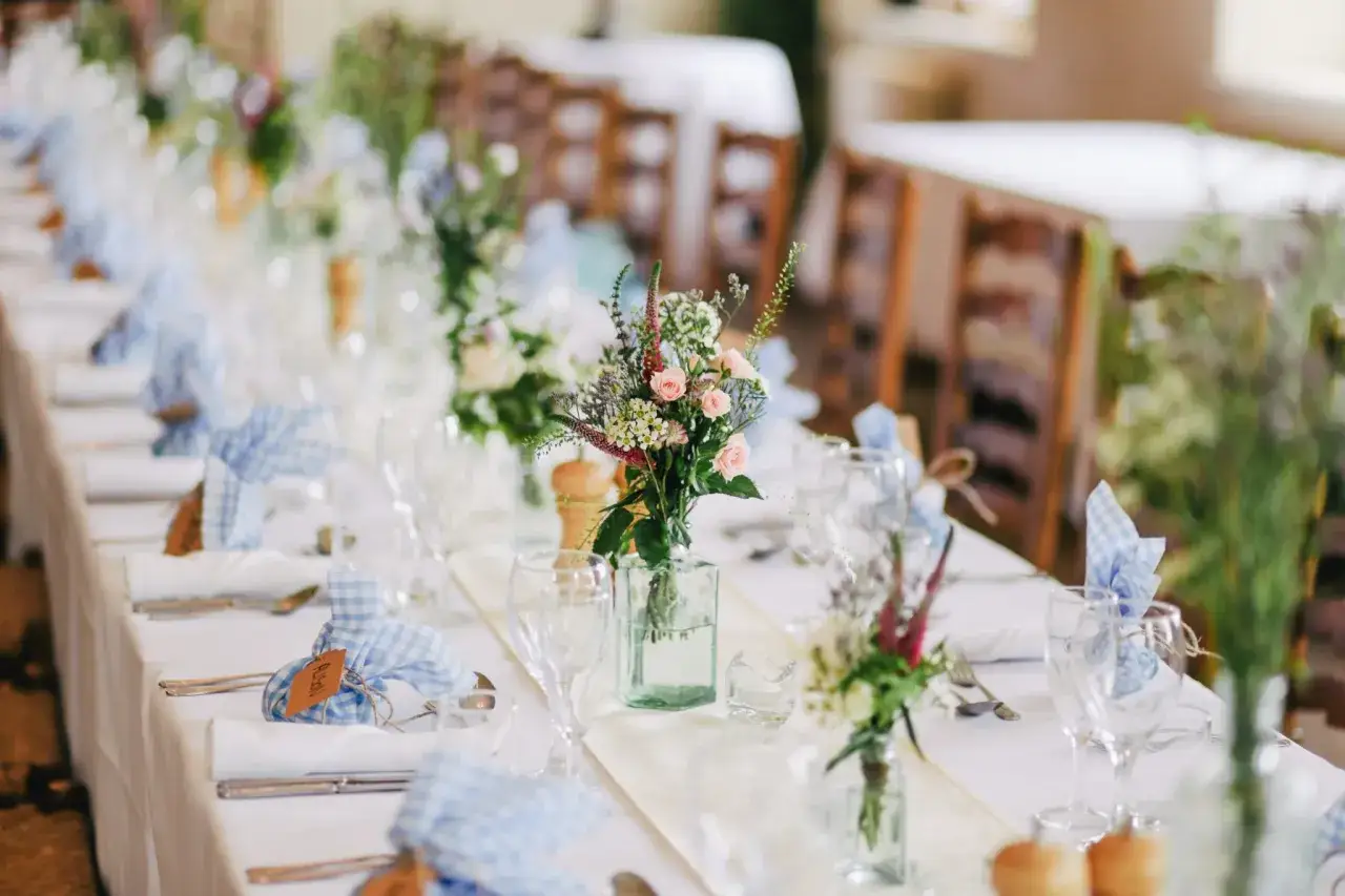 Décoration de table pour un mariage champêtre : bouquets de fleurs, serviettes à carreaux bleus, vaisselle. Une belle inspiration pour comment préparer un mariage.